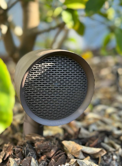 A speaker is sitting in the dirt next to a tree.