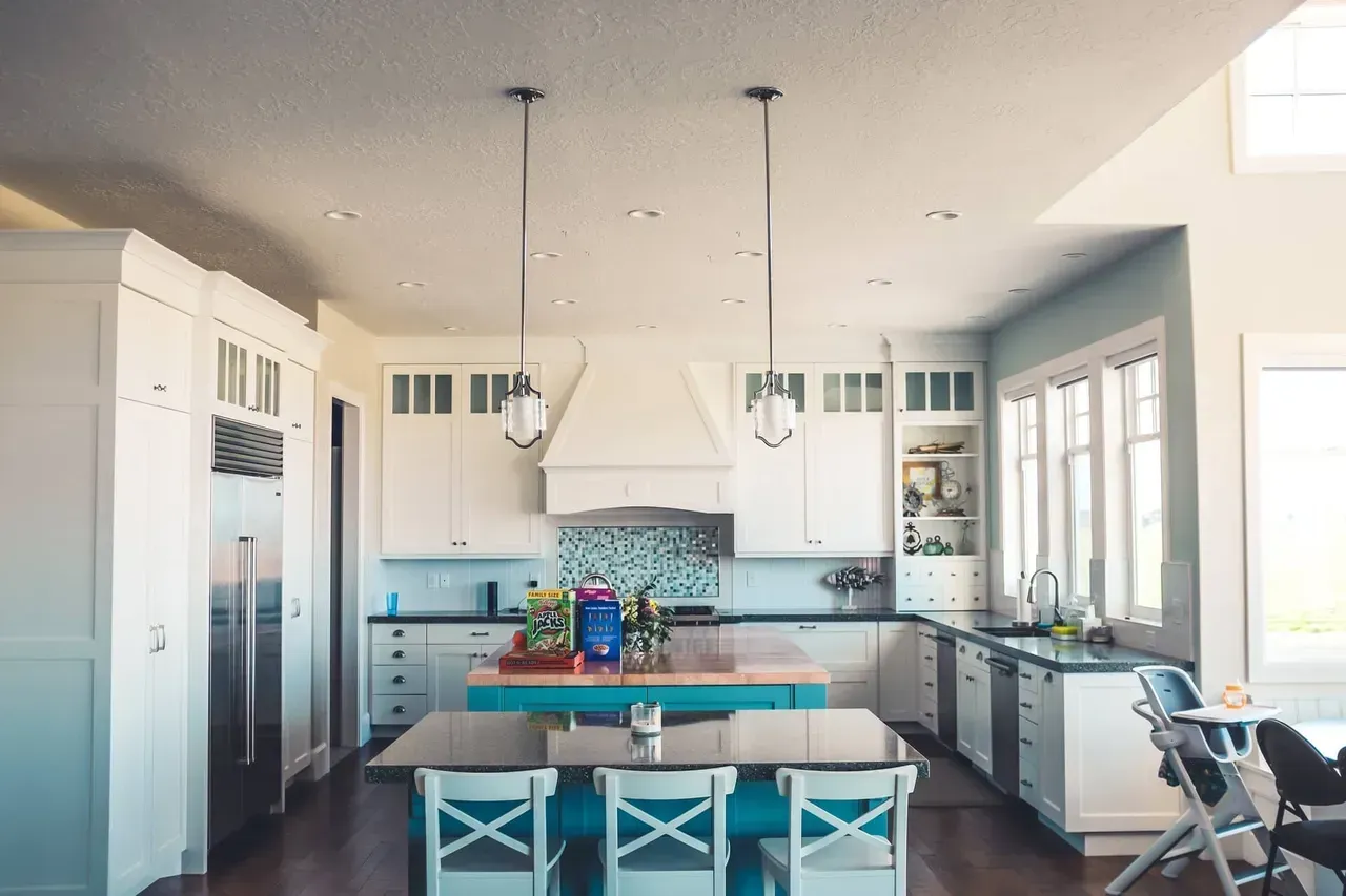 A kitchen with white cabinets , a blue island , a table and chairs.