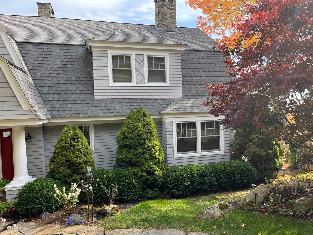 Gray house with gray roof, red door, and colorful fall foliage.