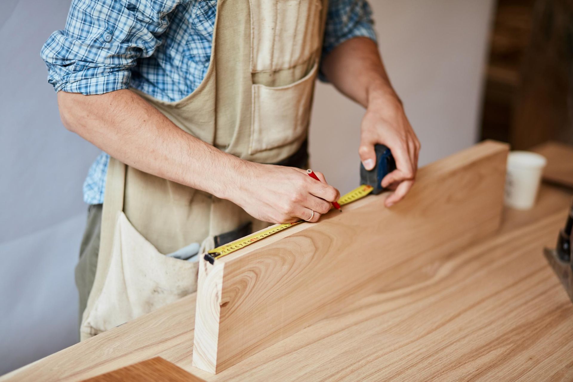 A man is measuring a piece of wood with a tape measure.