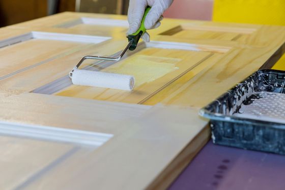 A person is painting a wooden door with a paint roller.