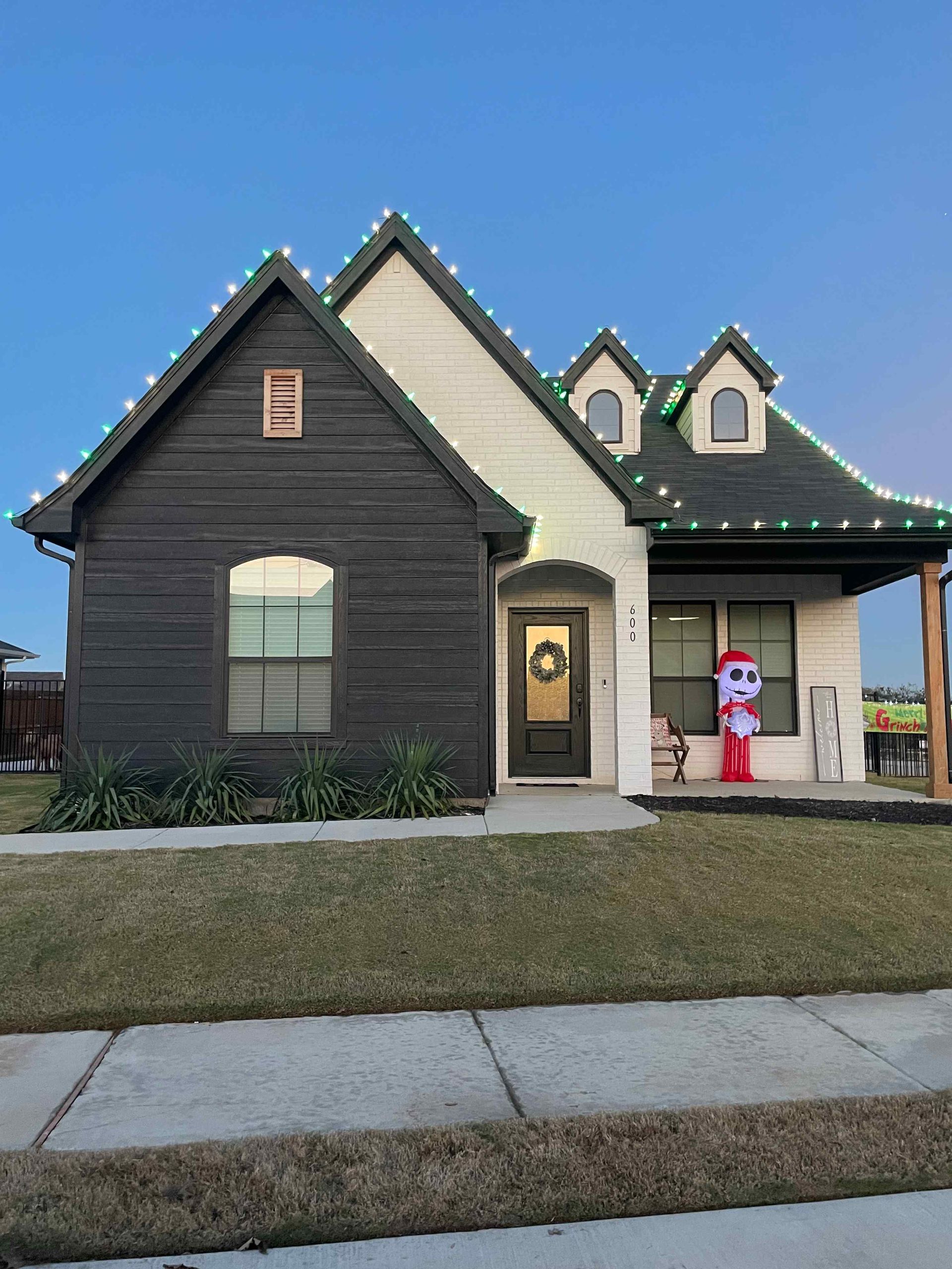 House decorated with Christmas lights, dark grey siding, white trim, and a Santa inflatable on the porch.