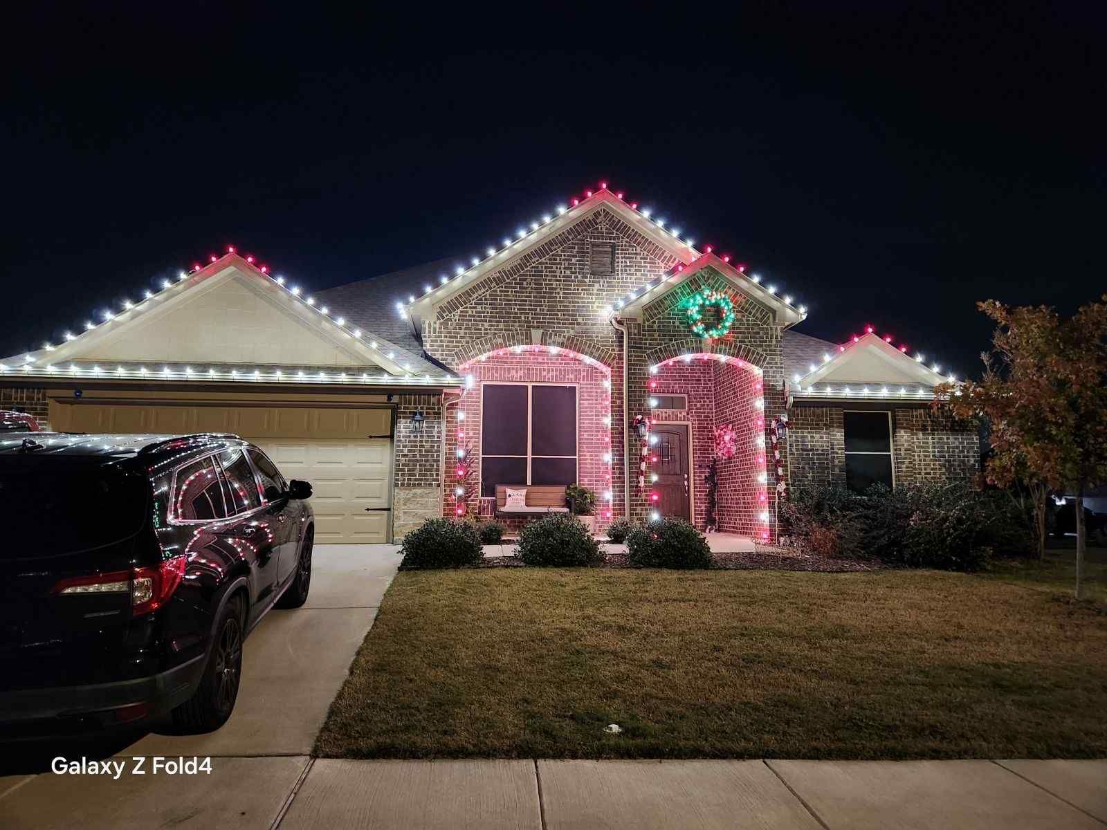 A house decorated with Christmas lights at night. Red and white lights trim the roof, door, and windows.
