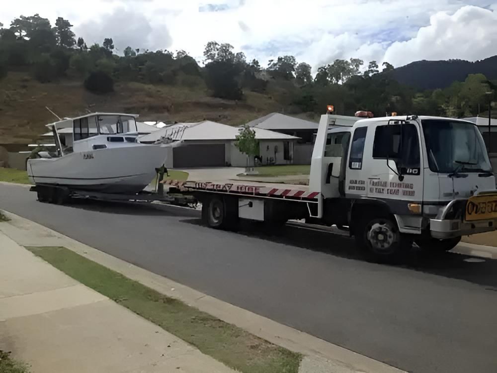 A Tow Truck is Carrying a Boat Down a Street — Airlie Towing & Tilt Tray Hire In Cannonvale, QLD