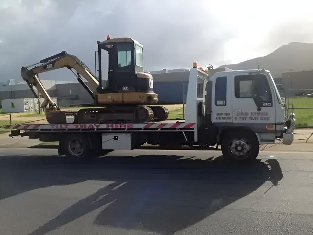 A Tow Truck With an Excavator on the Back of It — Airlie Towing & Tilt Tray Hire In Cannonvale, QLD