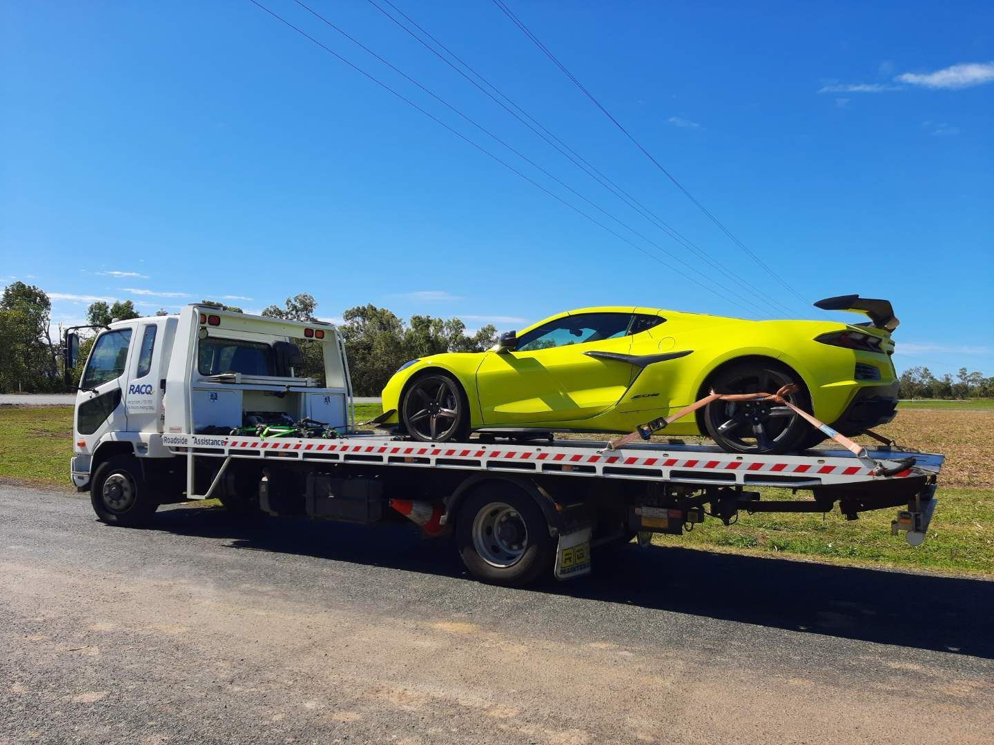 Bright yellow sports car strapped on a flatbed tow truck under a clear blue sky — Airlie Towing & Tilt Tray Hire In Proserpine, QLD
