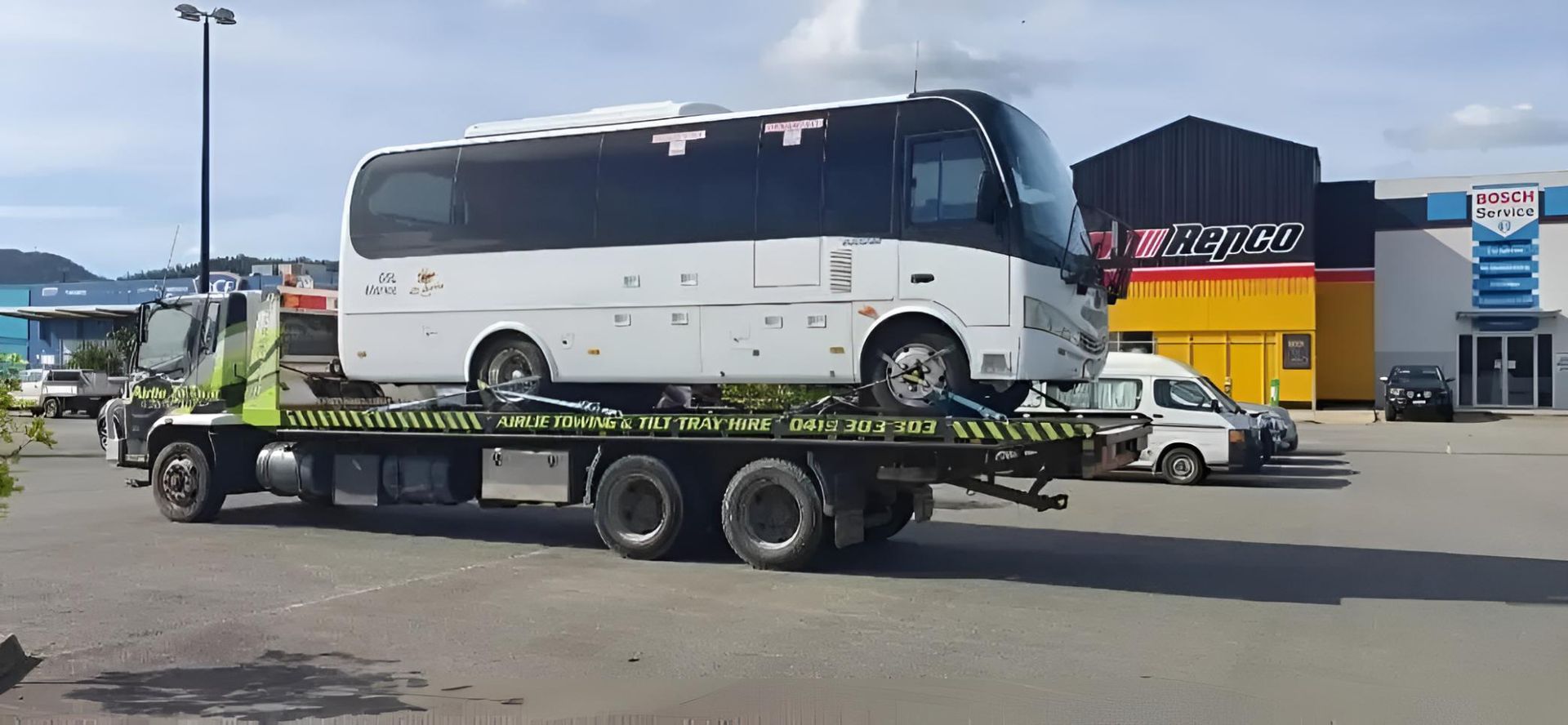 A Bus is Being Towed by a Tow Truck in a Parking Lot — Airlie Towing & Tilt Tray Hire In Cannonvale, QLD