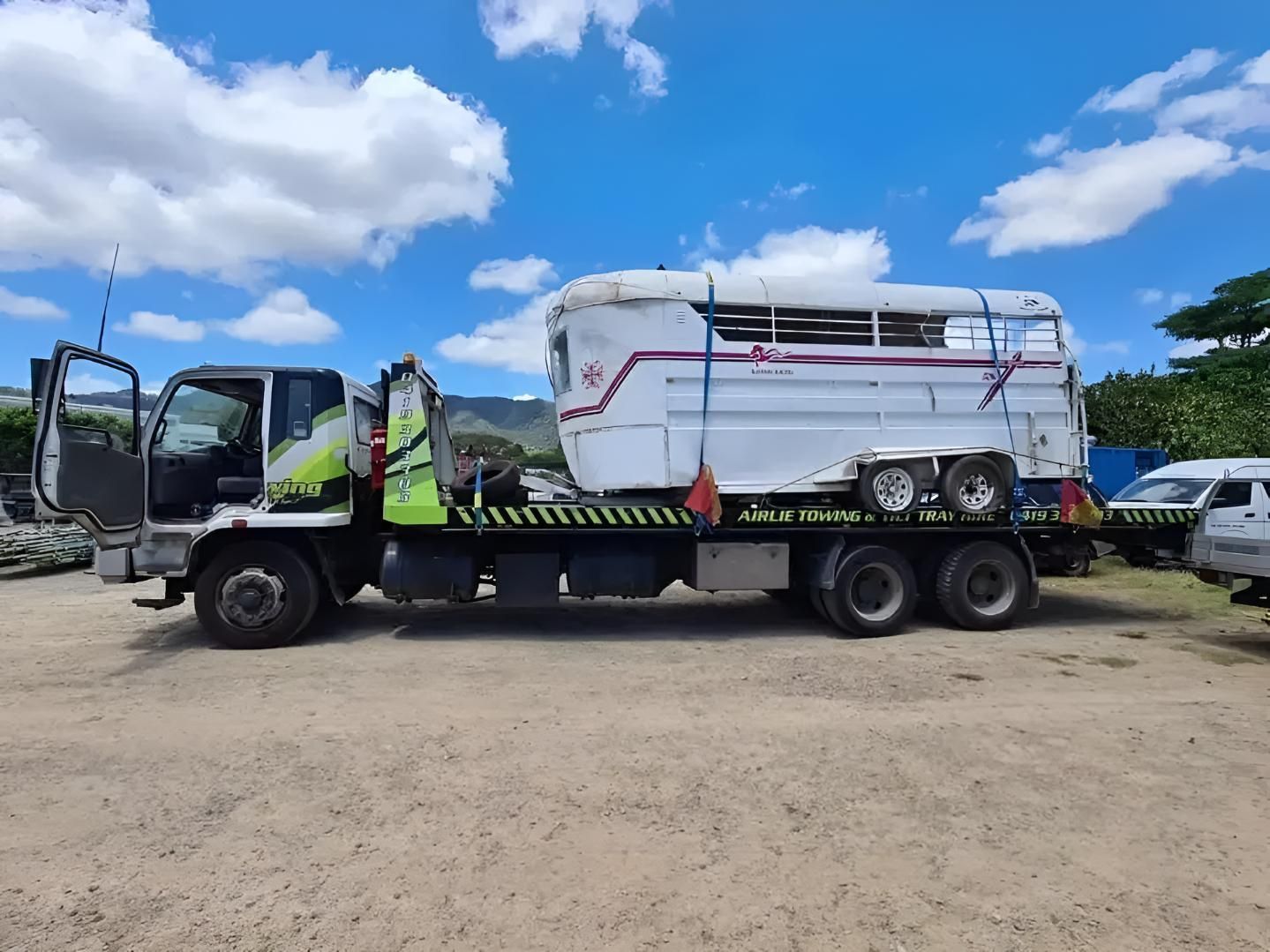 A White Truck With a Trailer Attached to It is Parked in a Dirt Lot — Airlie Towing & Tilt Tray Hire In Cannonvale, QLD