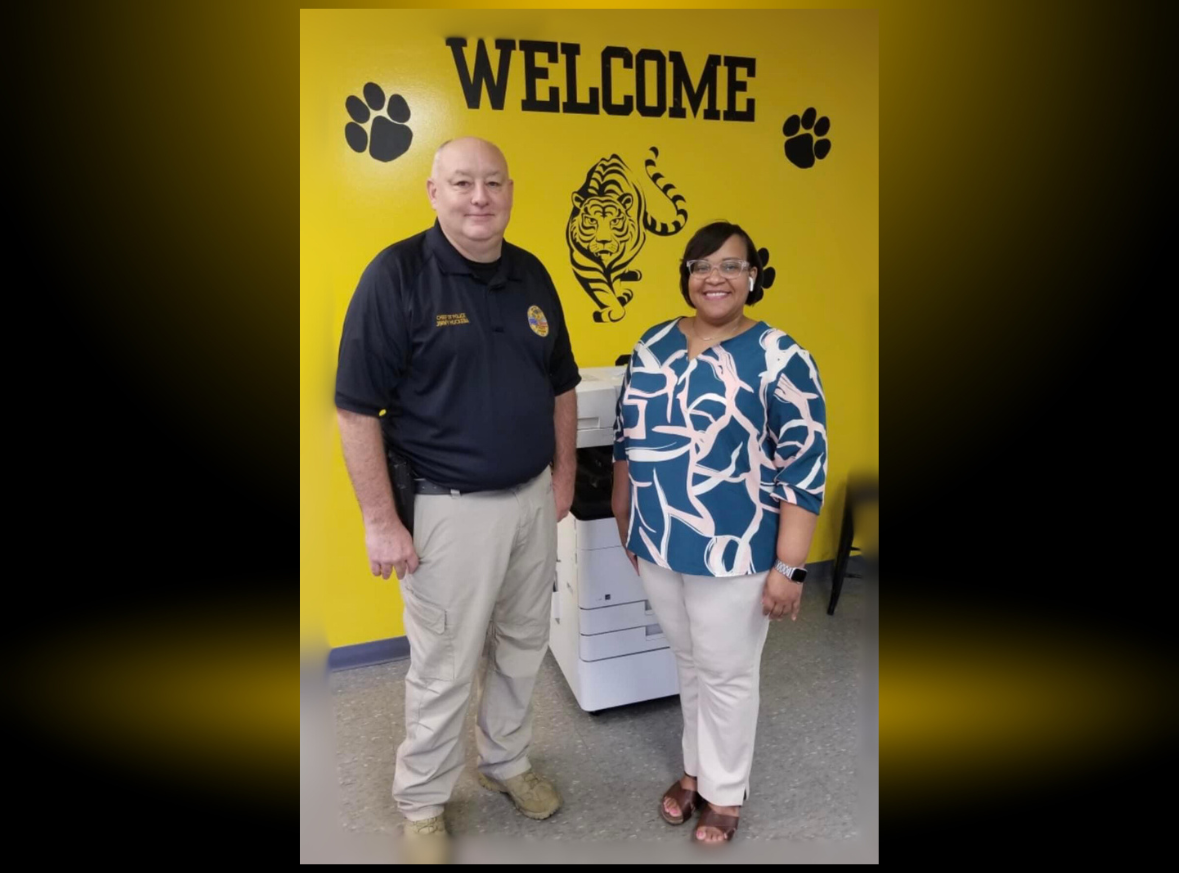 a man and a woman are standing in front of a yellow wall that says welcome