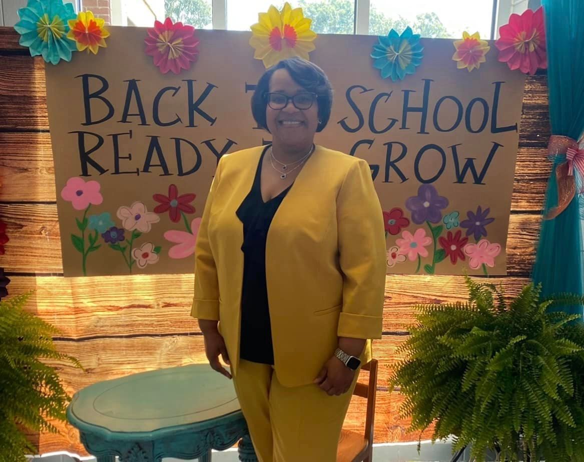 a woman in a yellow suit is standing in front of a sign that says back to school ready grow