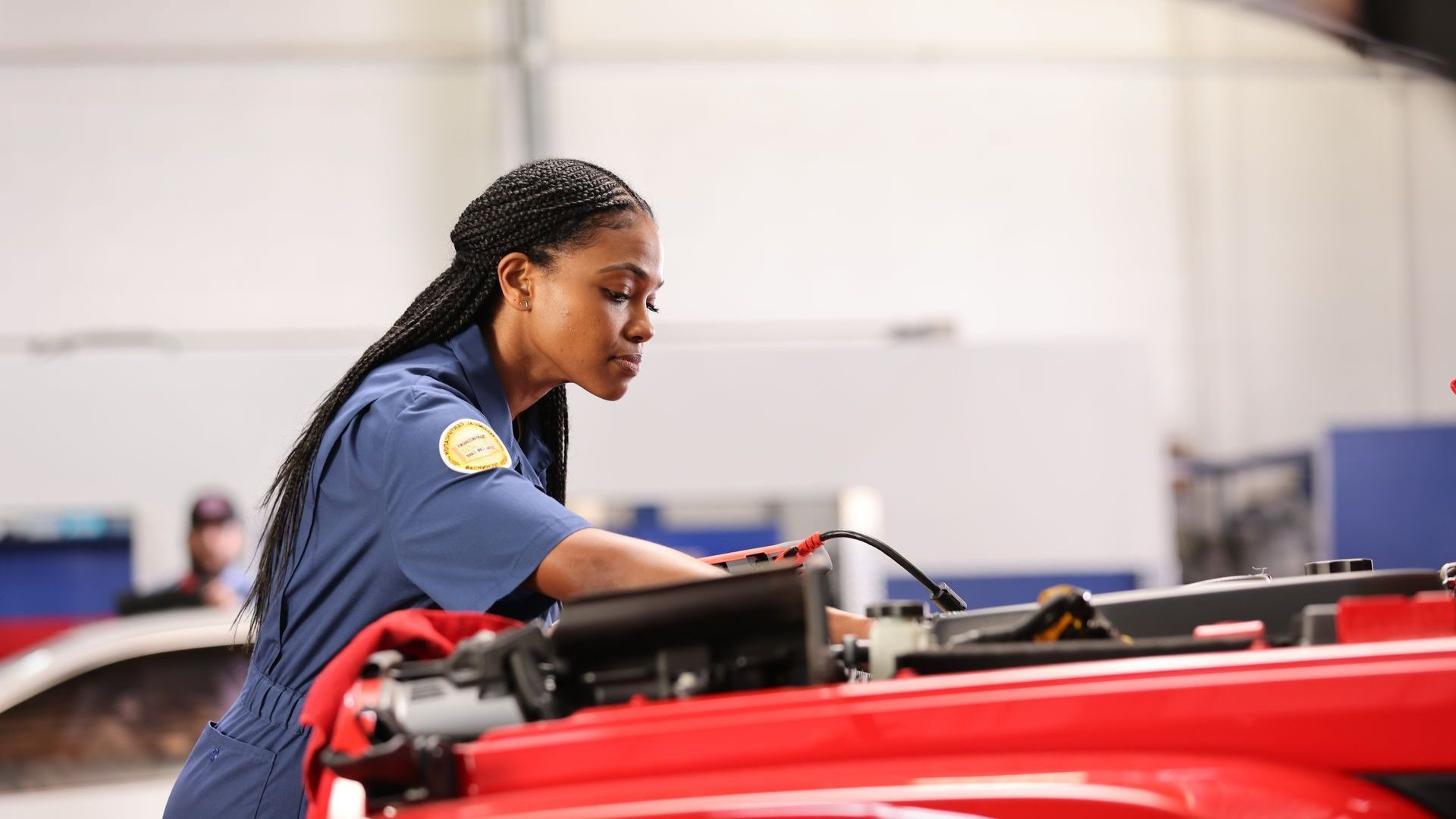 Person in blue uniform leaning over a red vehicle in a workshop, inspecting or working on it.