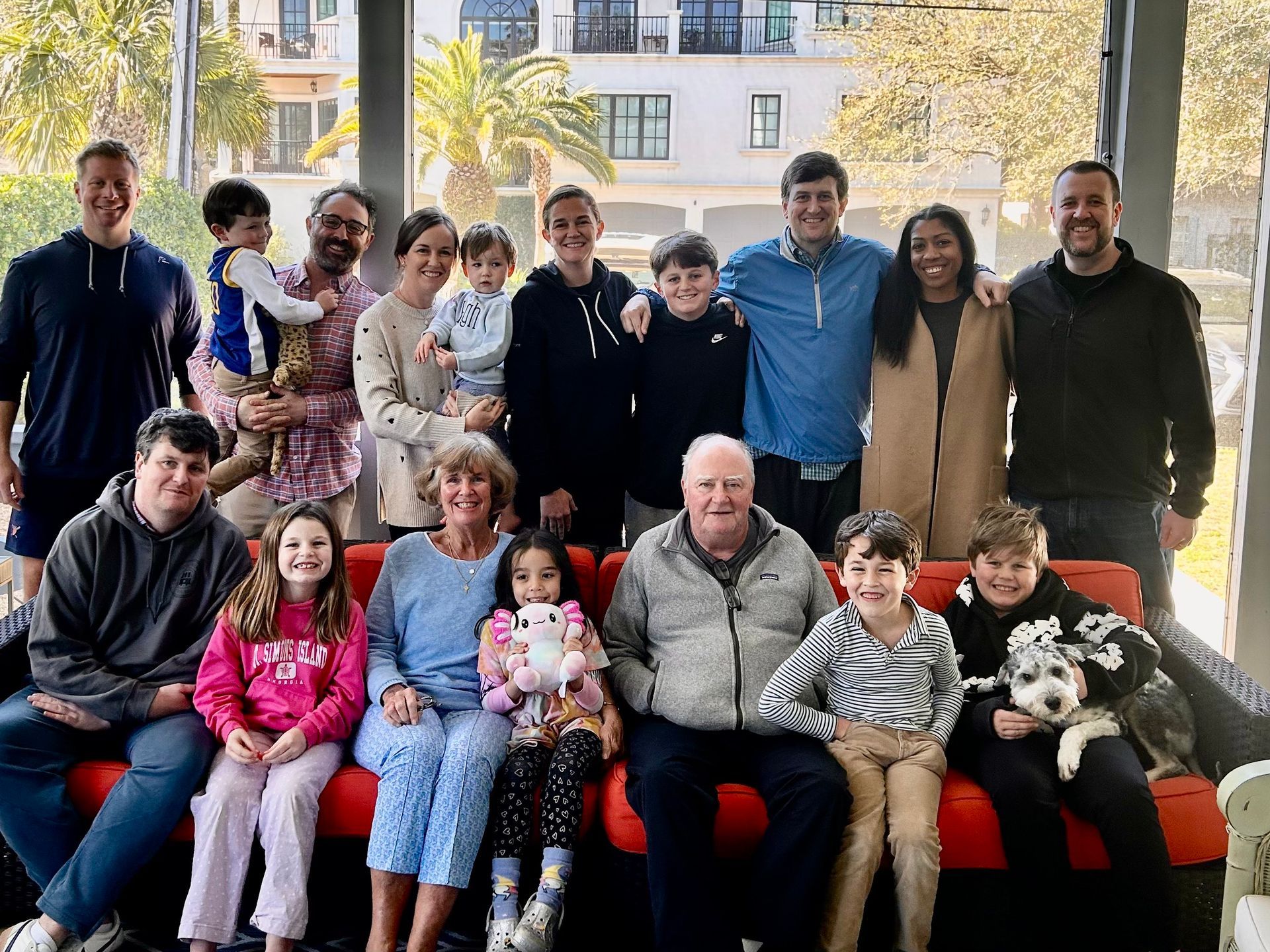 Family group portrait on a red couch, with a window and palm trees in the background.