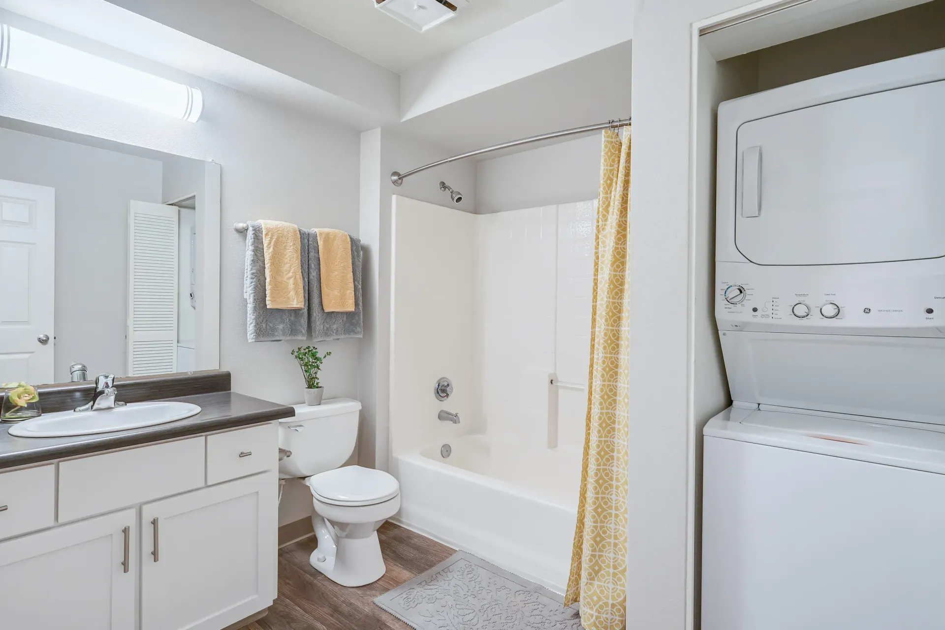 Bathroom in an apartment with a vanity, toilet, bathtub/shower, and a stacked washer/dryer.