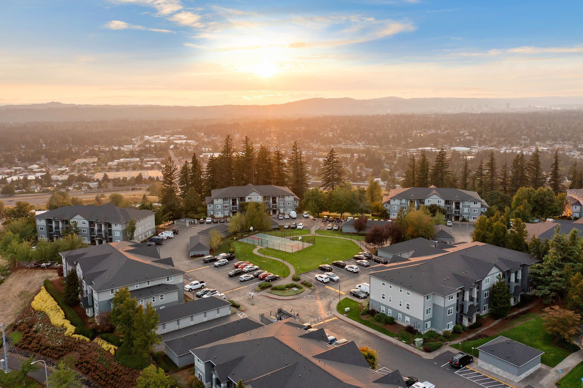 Aerial view of a multi-building apartment community with parking and central green space at sunset.