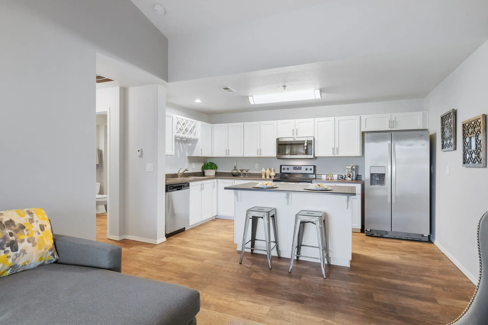 Open-concept kitchen with white cabinets, stainless-steel appliances, and a central island with two metal stools.