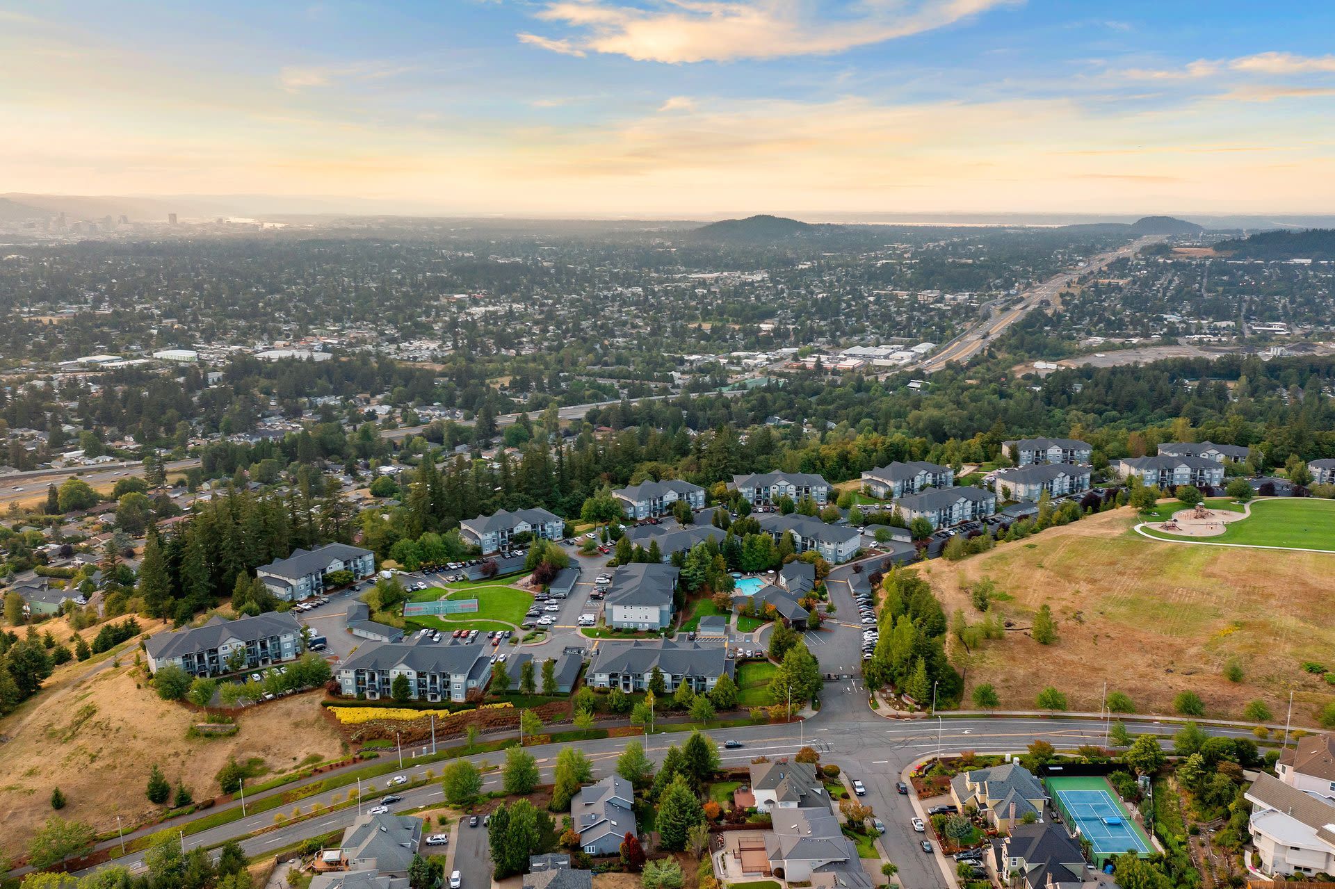 Aerial view of a suburban apartment community with multiple buildings, green spaces, and a tennis court.