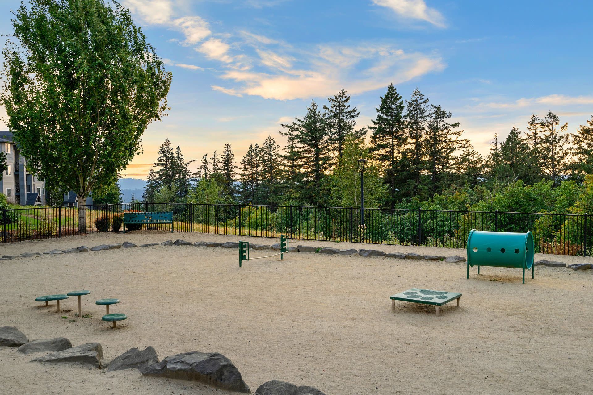 Outdoor community playground with sand, climbing equipment, and a fence.