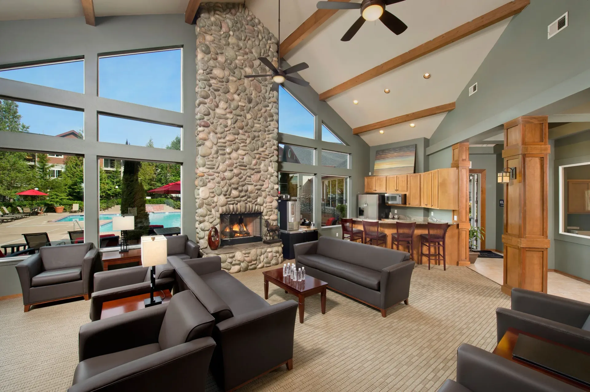Interior of a community lounge with a stone fireplace, high ceilings, and large windows.