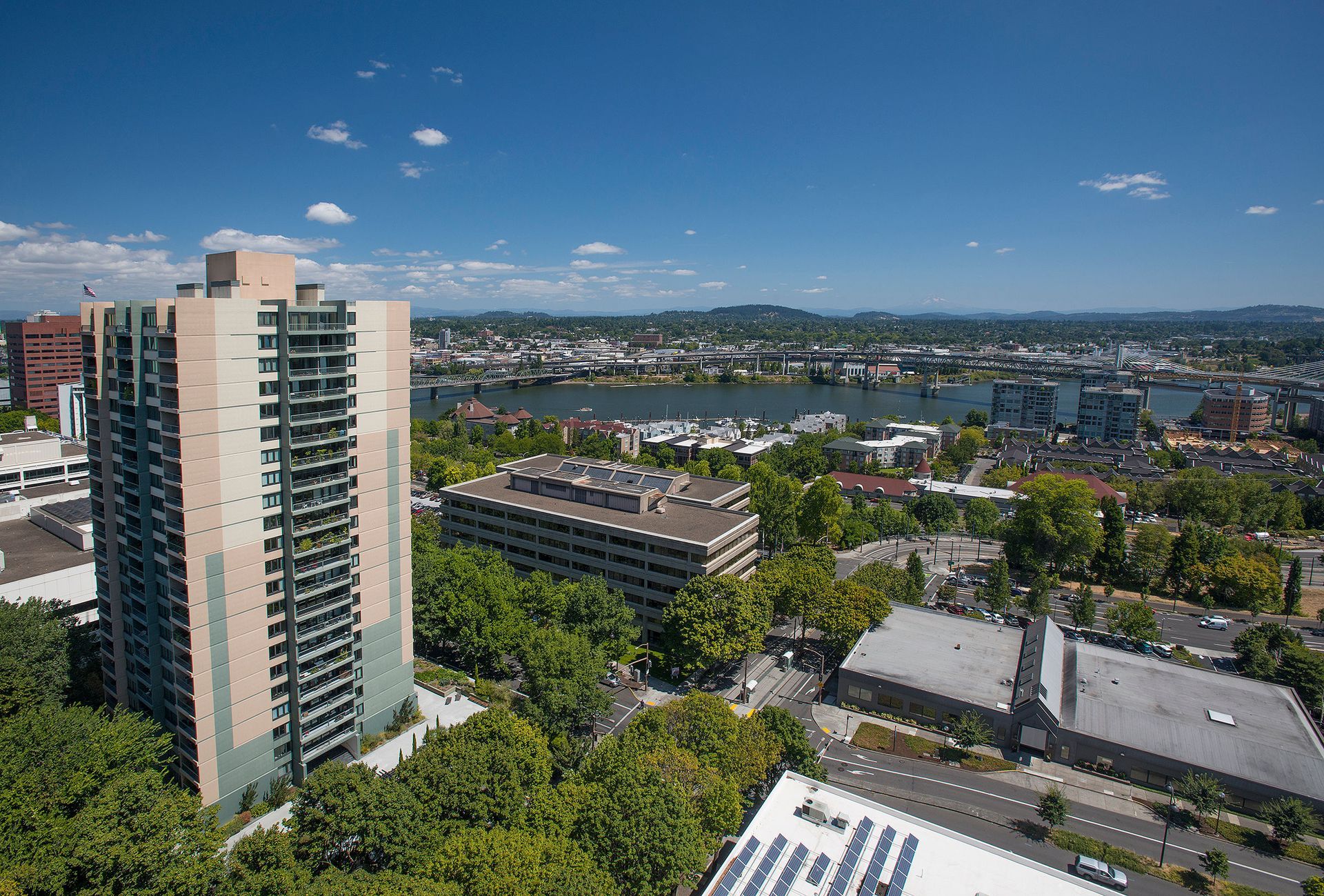Aerial view of a tall apartment tower and surrounding cityscape by a river with bridges.