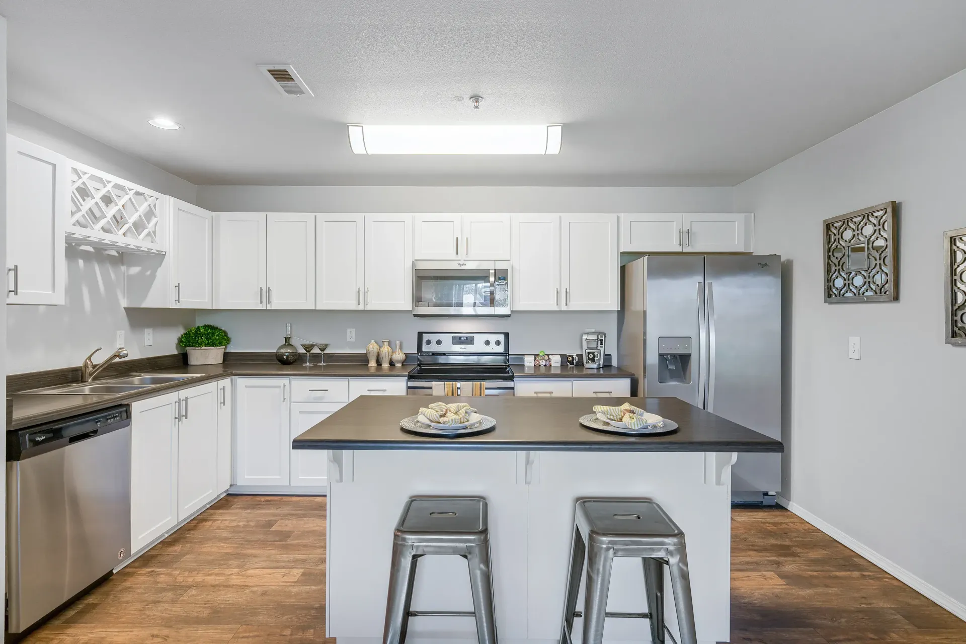 Bright modern kitchen with white cabinets, stainless steel appliances, and an island with two metal stools.