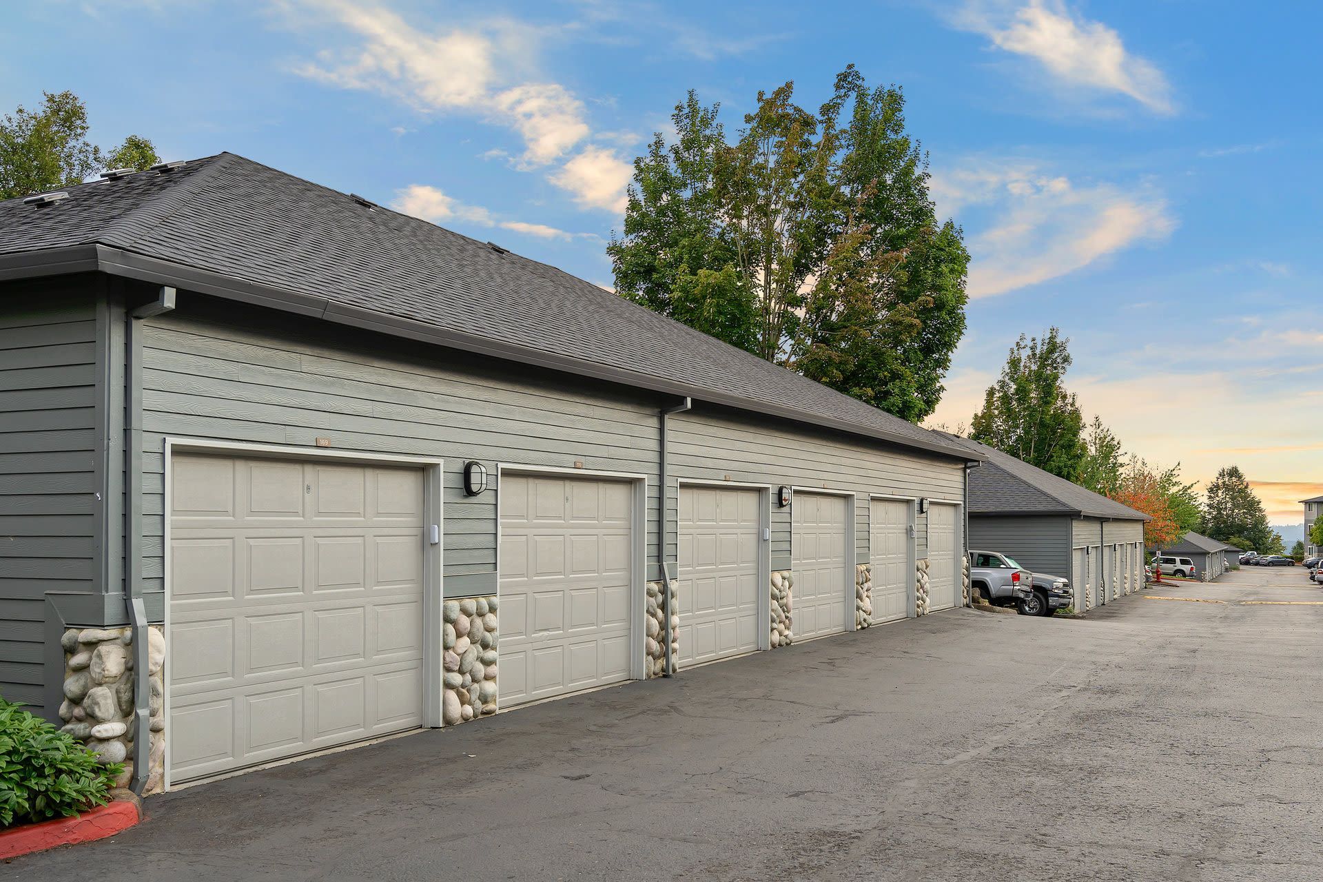 Row of gray garage doors along a multi-family building with stone column accents and a paved lot.