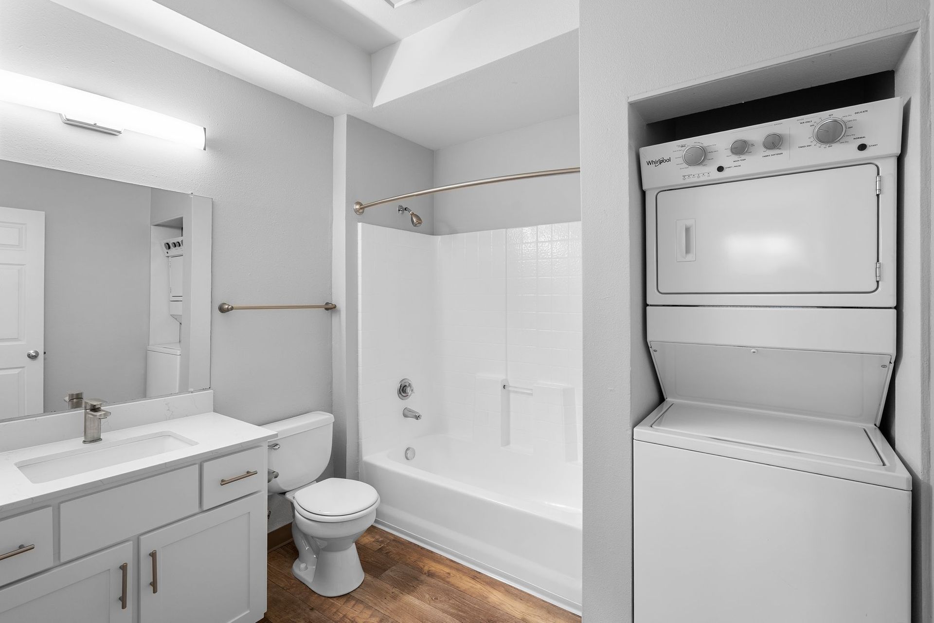 A bathroom featuring a white vanity sink, toilet, tub-shower combination, and a stacked white washer and dryer unit.