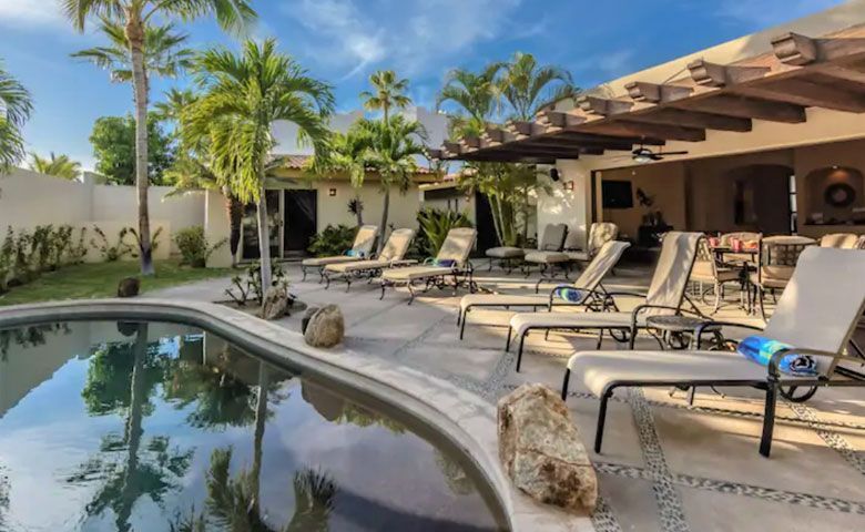 A large swimming pool surrounded by lounge chairs in front of a house.