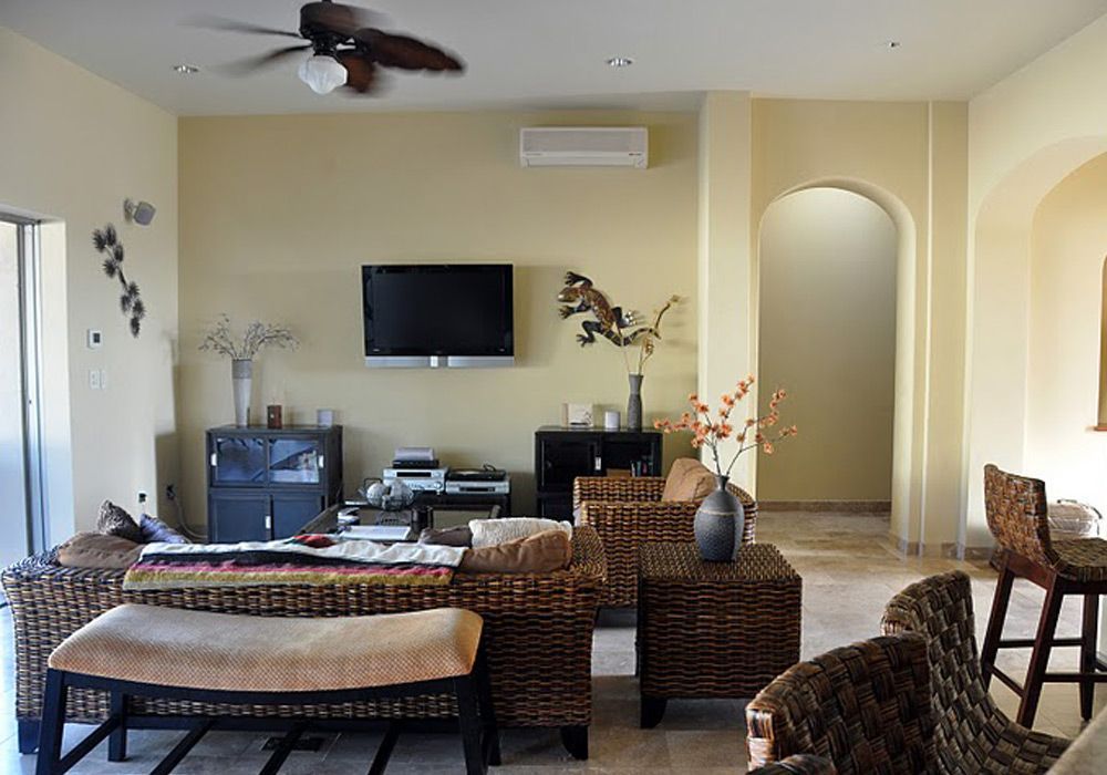 A living room with wicker furniture , a flat screen tv and a ceiling fan.