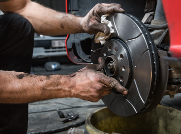Mechanic cleaning a car brake rotor with a cloth; setting is a garage. | Zee's Alignment & Autocare