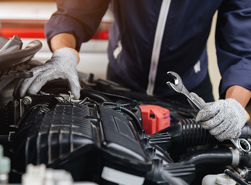 Mechanic in blue coveralls and gloves working on a car engine with a wrench. | Zee's Alignment & Autocare