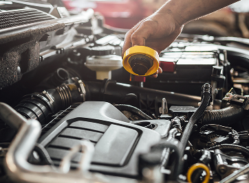 Person checking car engine oil with yellow cap in an engine bay. | Zee's Alignment & Autocare