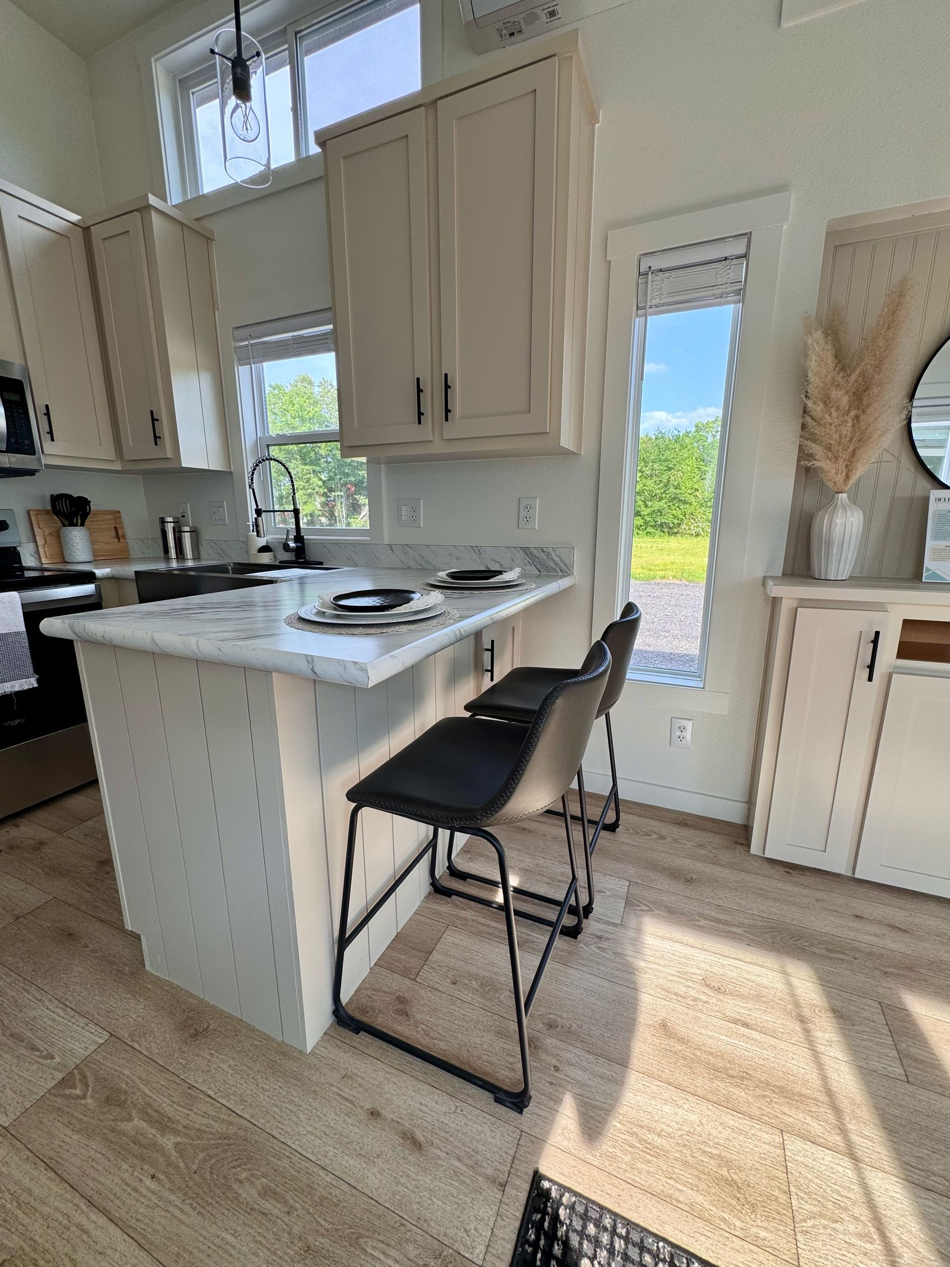 Kitchen with off-white cabinets, a small breakfast bar with two stools, and a window with a view.