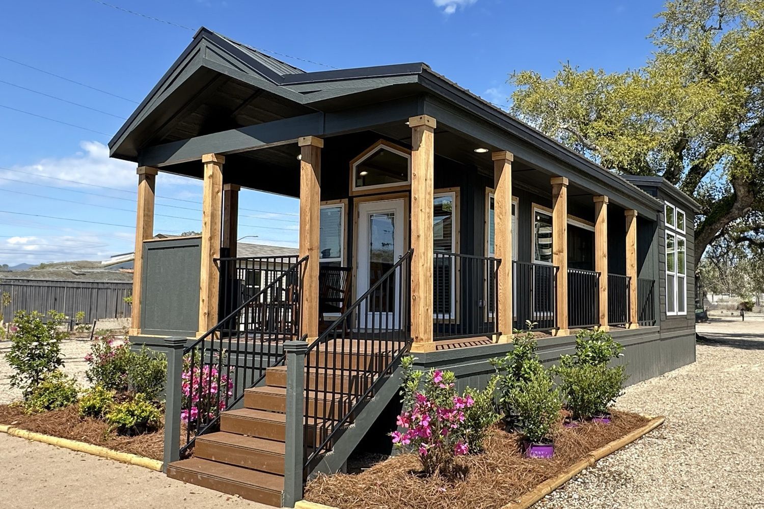 Gray tiny house with porch and steps, surrounded by landscaping.
