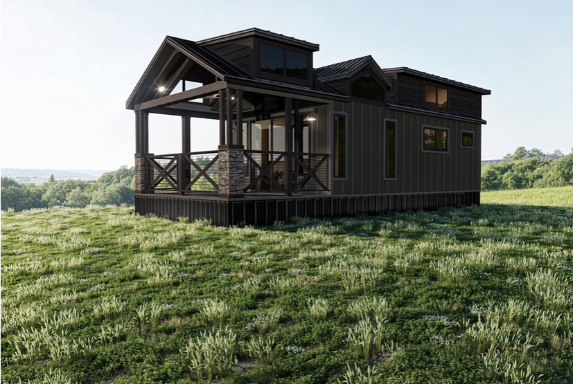 Dark-sided tiny house with porch and dormer windows, set on a grassy hill.