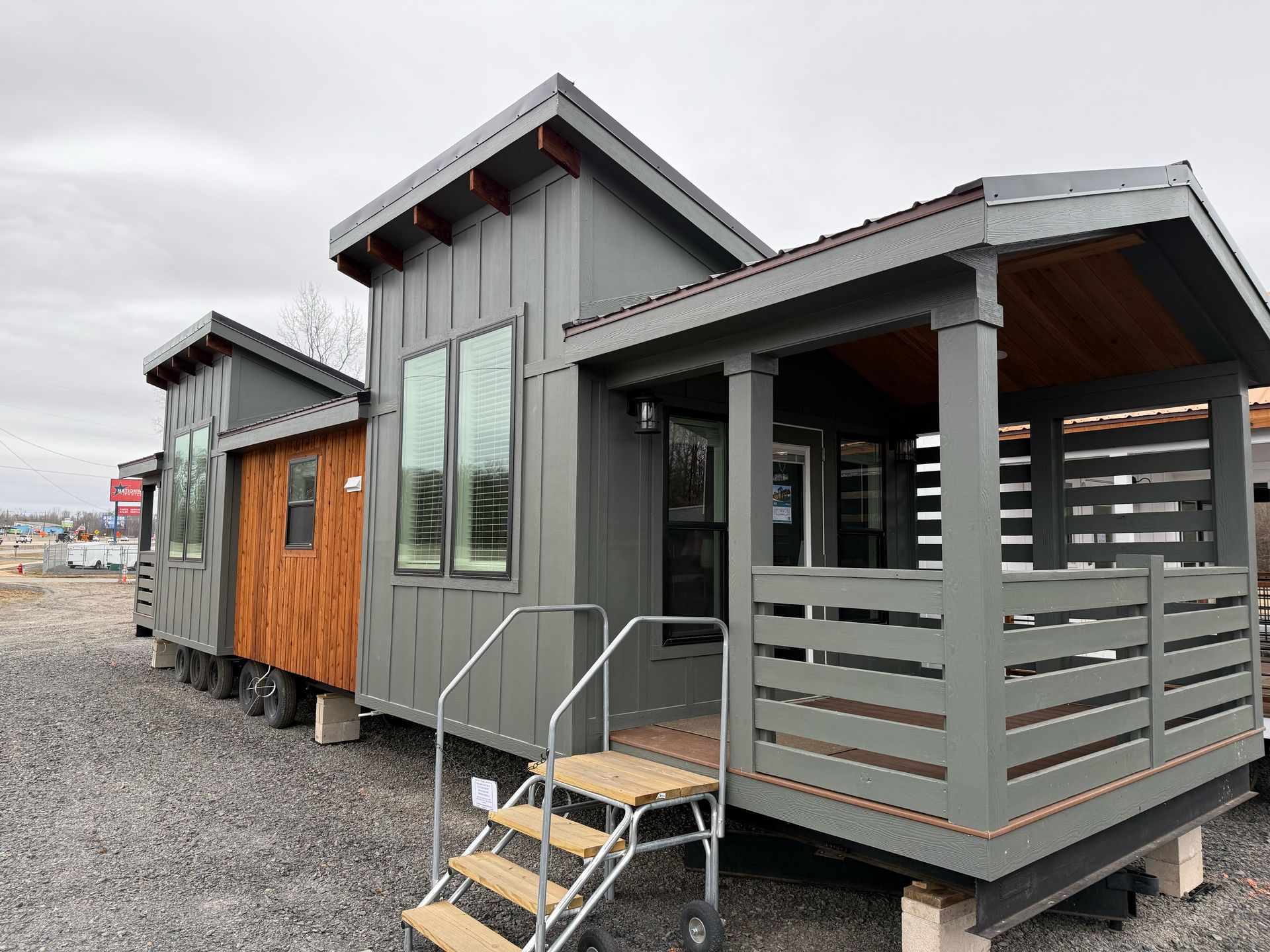 Tiny house with gray siding and a porch. The house is on wheels.