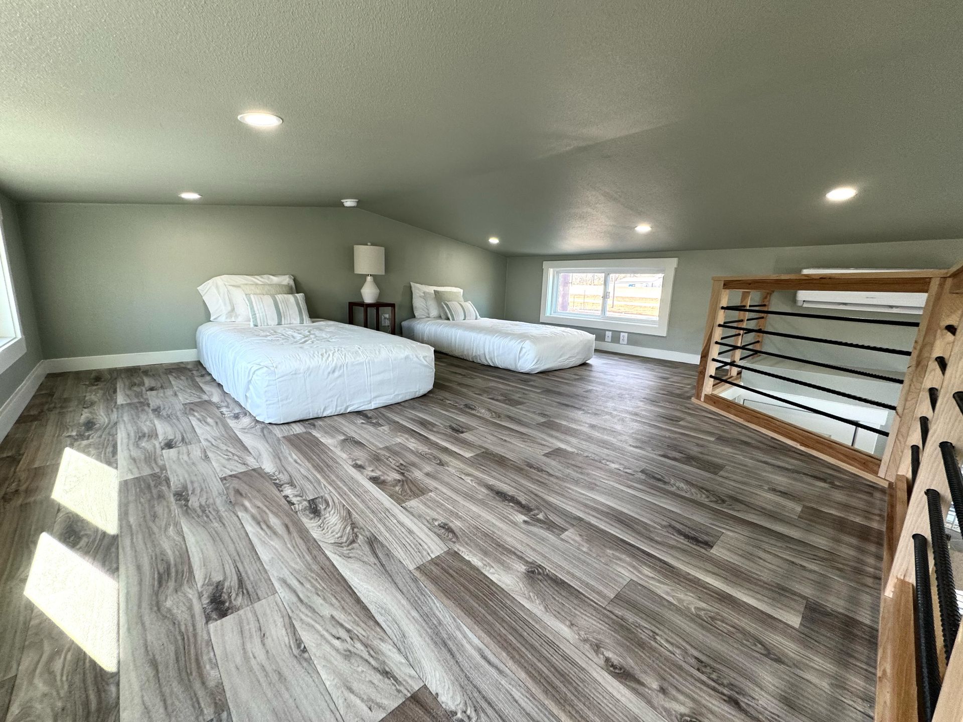Loft bedroom with two twin beds, wood floor, light green walls, and a window.