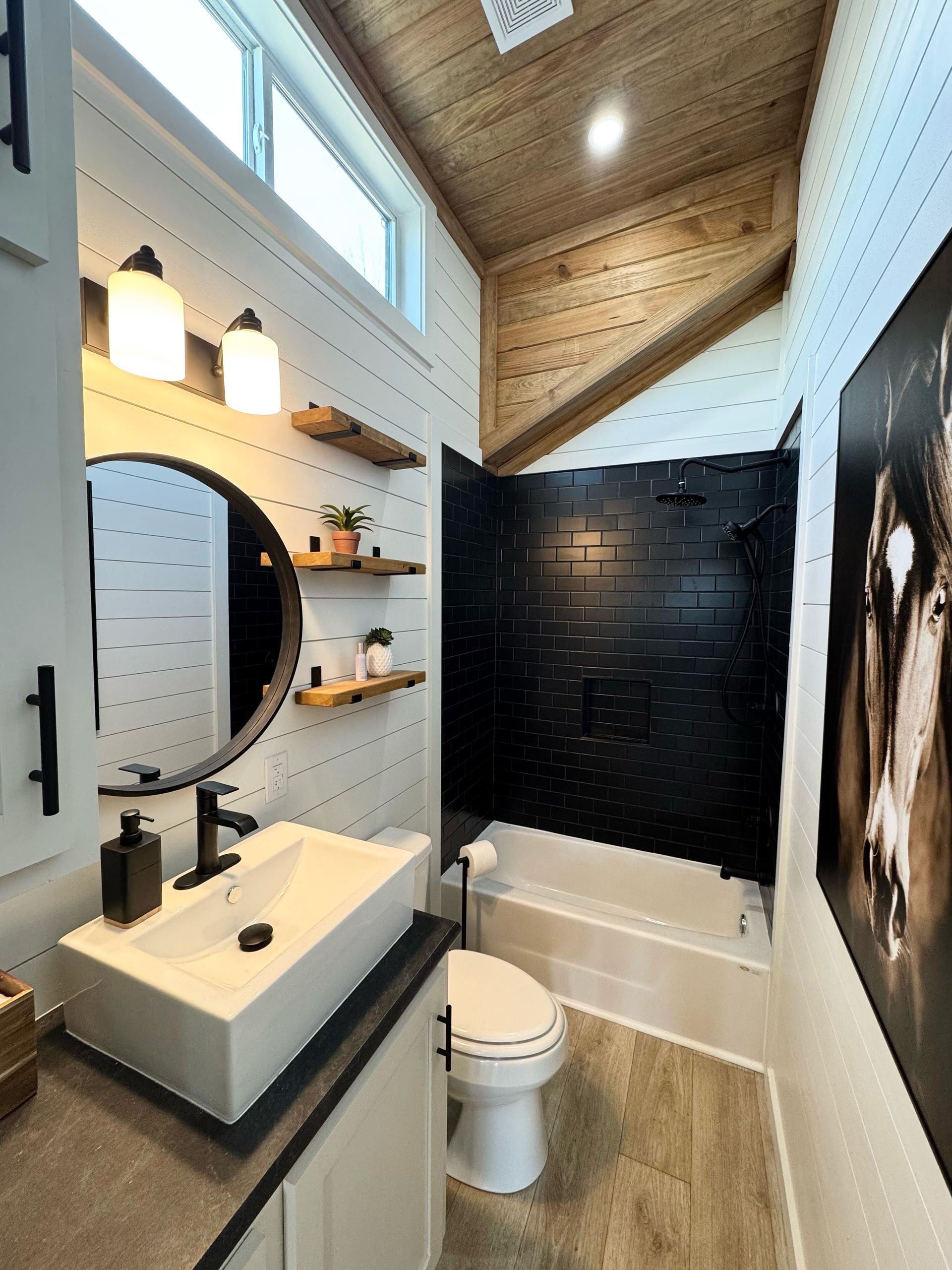 Bathroom with white sink, black accents, wooden ceiling, and a black-tiled shower.