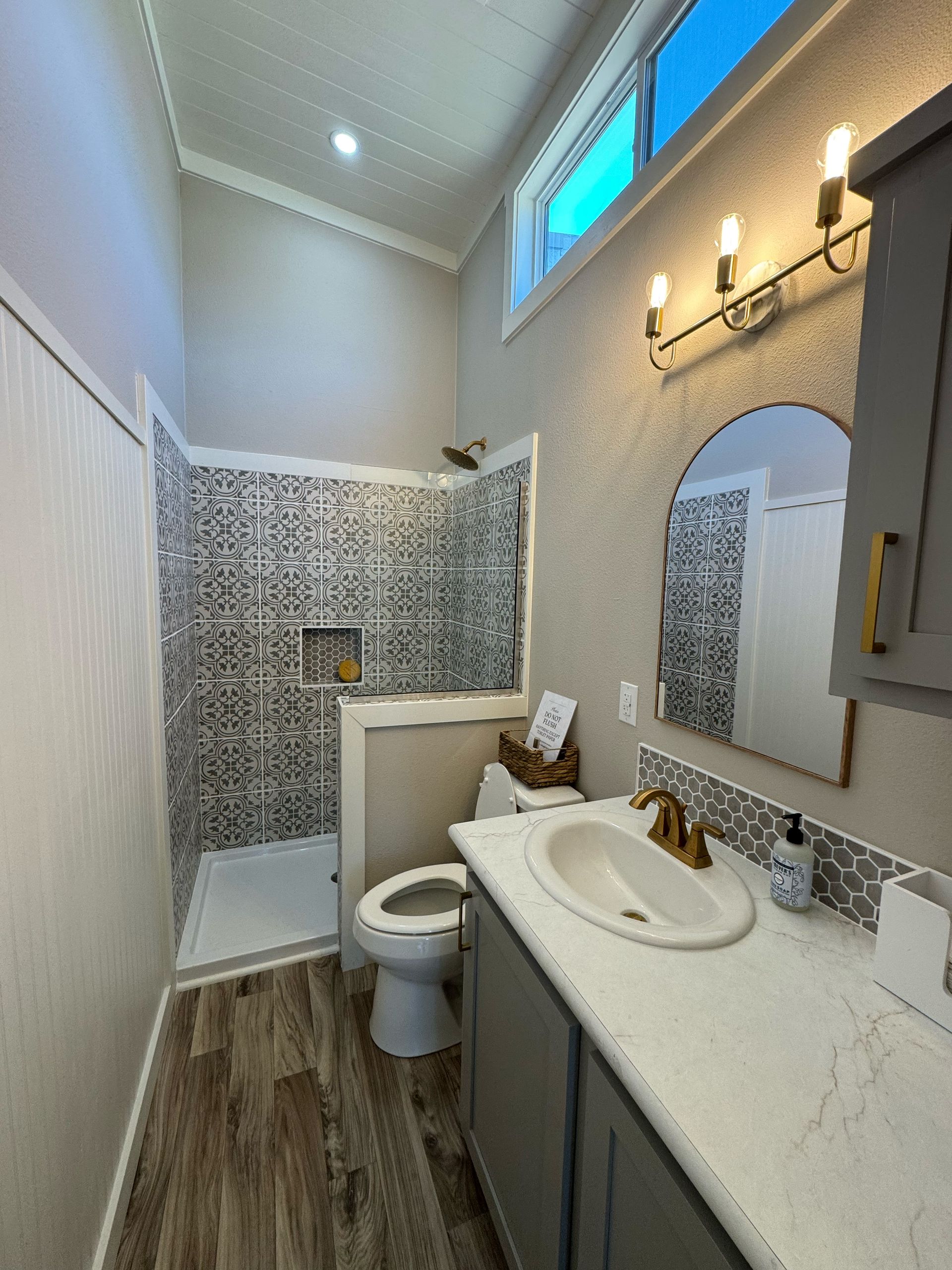 Bathroom with patterned shower tile, gray vanity, and a window.