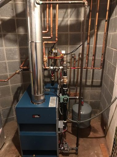 Boiler room with blue furnace, copper pipes, and a silver vent tank in a tiled utility alcove