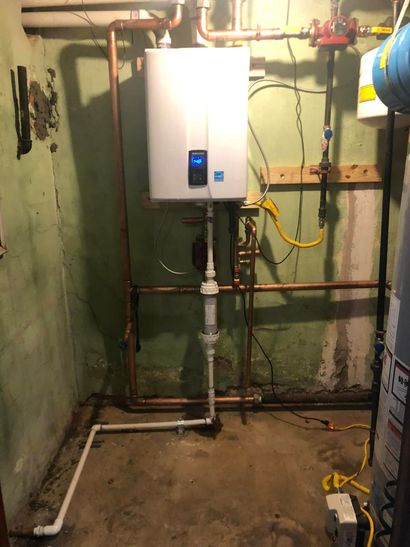 Wall-mounted water heater with exposed pipes in a utility basement room.