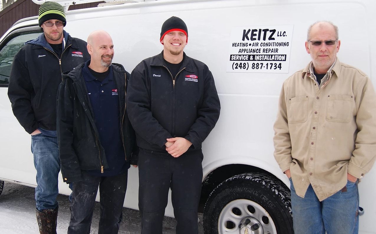 Four men standing beside a white utility van in the snow, one with a company logo on the side.