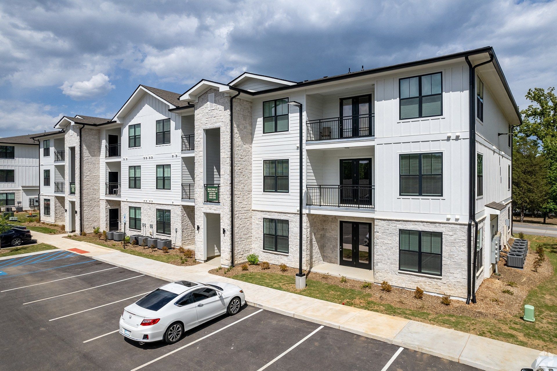 Dog-Friendly Apartments in Hixson, TN - Ridgeview at Northgate - Exterior View of Property with White Walls, Stone Details, Black Trim, Windows, and Parking Area.