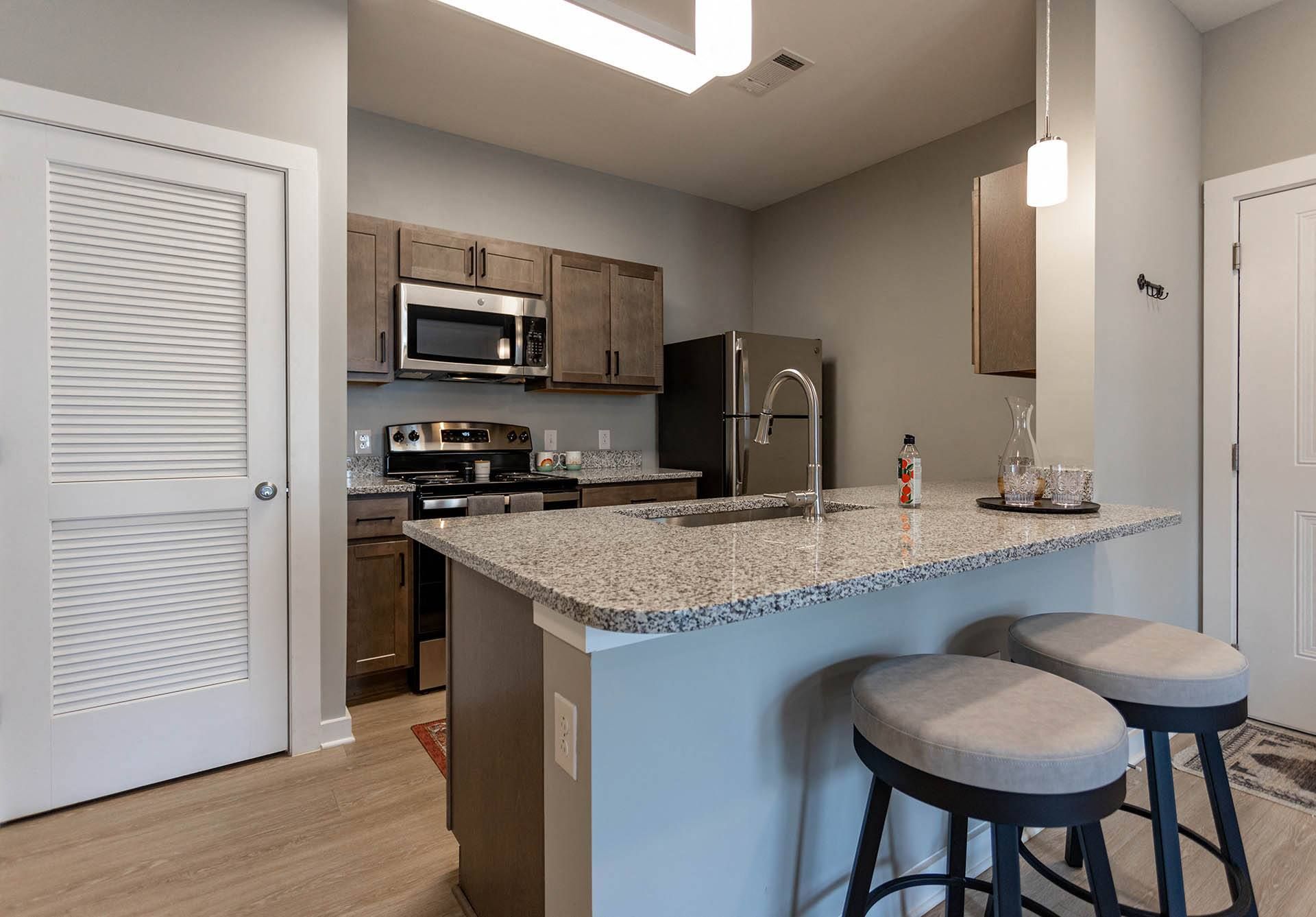 Pet-Friendly Apartments in Hixson, TN - Ridgeview at Northgate - Kitchen with Luxury Vinyl Plank Floor, Granite Countertops, Stainless Steel Appliances, Wood-Tone Cabinets, Peninsula with Stool Seating, and Pendant Lights.