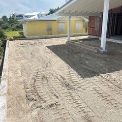 A dirt driveway with tire tracks, next to a building under construction and a yellow house.