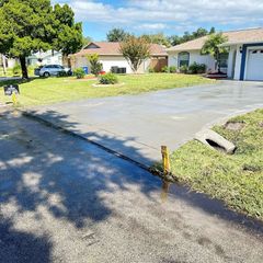 Driveway with water runoff into grass, sunny day. Homes in background.
