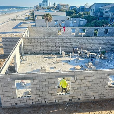 Construction of concrete block buildings near a beach. A worker stands in a doorway, several unfinished structures visible.