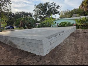 Concrete block foundation on dirt, likely for a building, with trees and houses in the background.