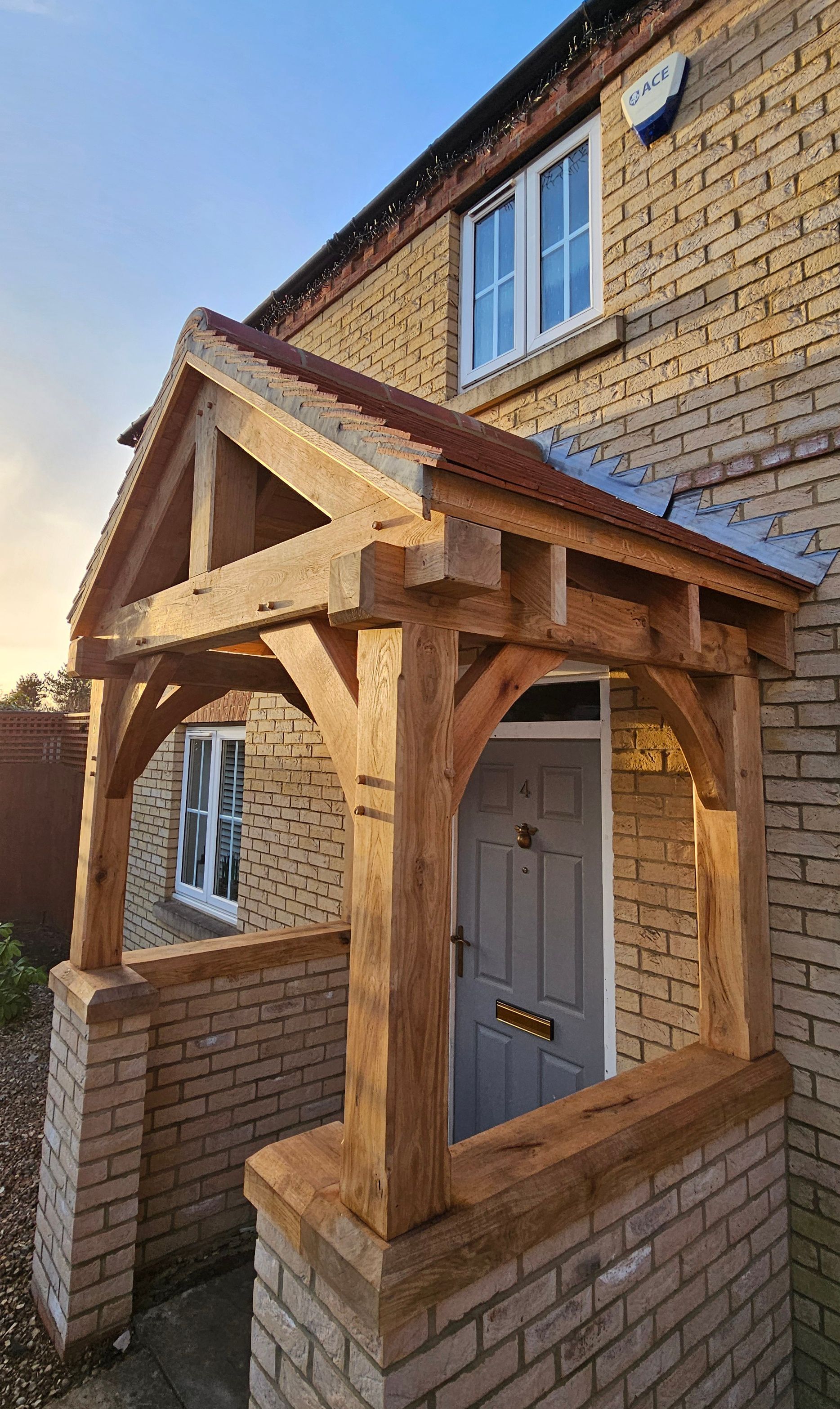 A newly installed oak timber porch over a grey front door, attached to a brick house under a blue sky.