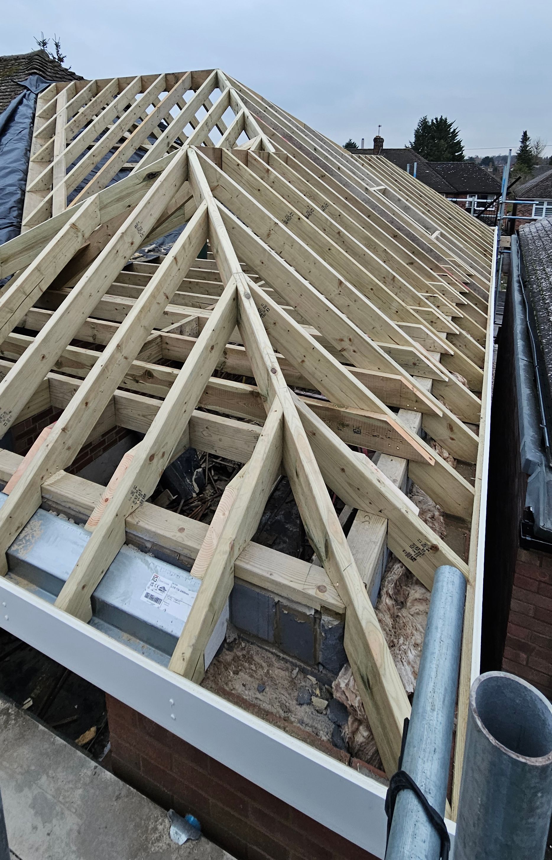 An angled view of a newly constructed wooden roof frame showing hand cut rafters, ridges, and hips on a building under renovation.