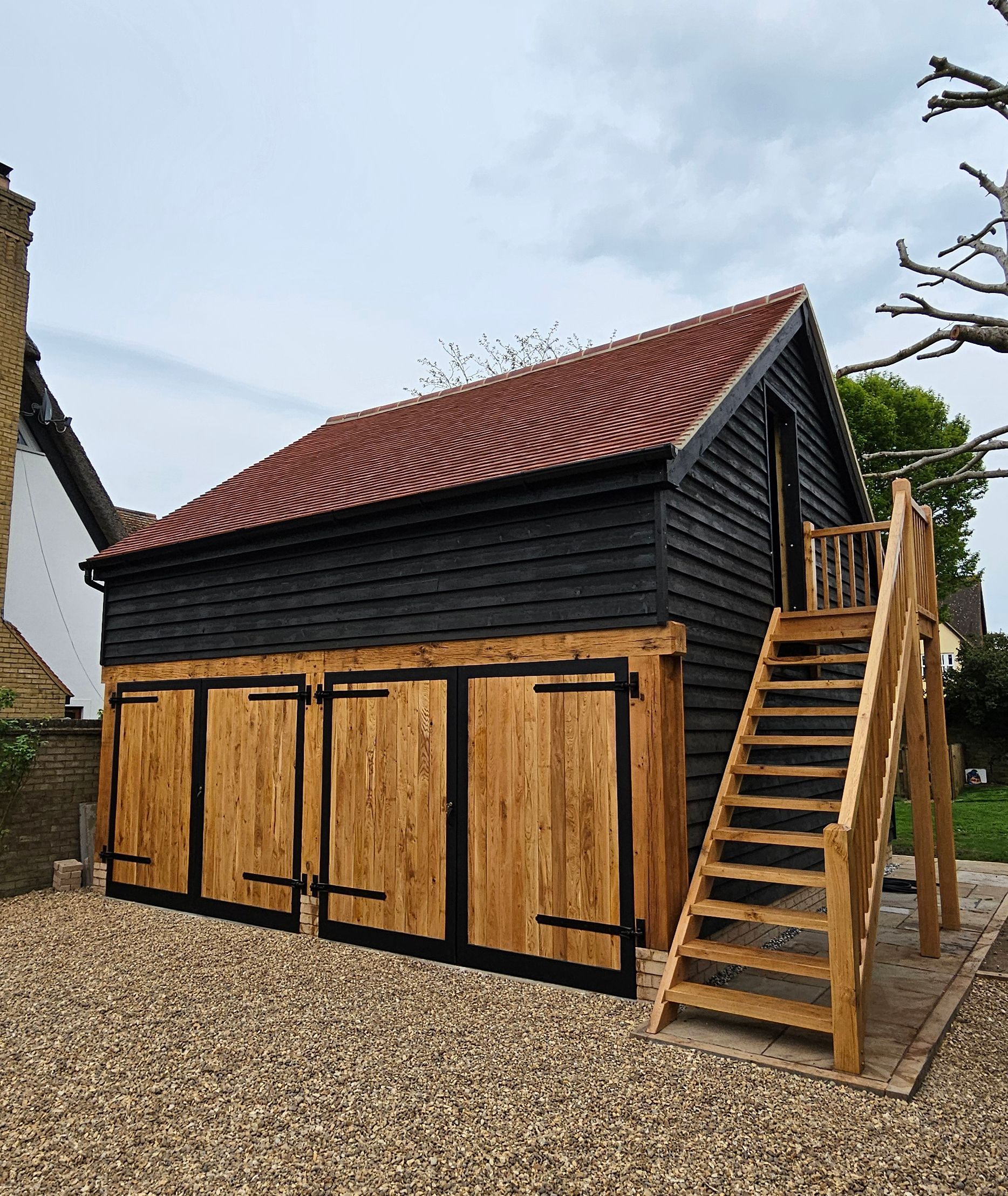 Oak frame garage with natural wood doors, red tiles roof, and an external oak staircase.